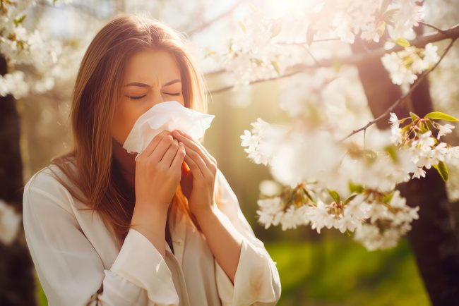 Frau steht neben einem blühenden Baum und schneuzt sich in ein Taschentuch