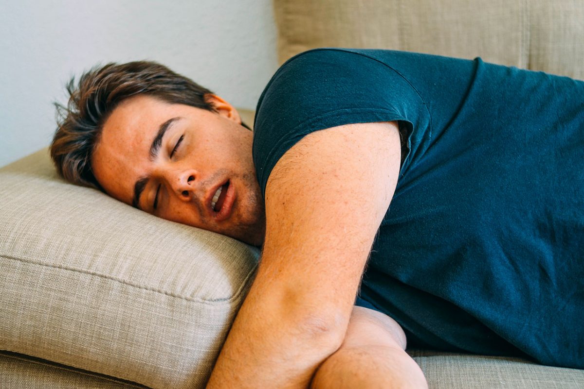 Mann liegt auf einem Sofa und schnarcht mit offenem Mund